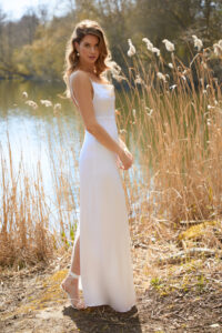 Stunning bride on a sunny riverbank in white dress.