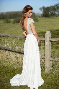 A beautiful bride in a field by a fence in white dress.
