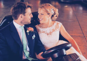 A pretty bride with beautiful hair and makeup in a dodgem car with her groom.