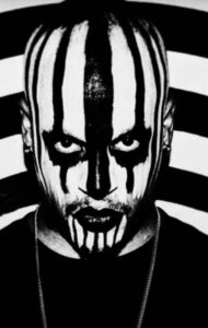 A man with stripey black and white facepaint over his whole head.