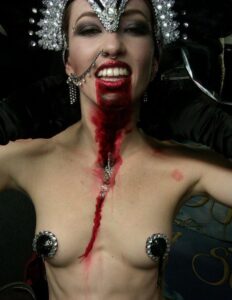 A model with Halloween makeup, crown and blood running down her chest.