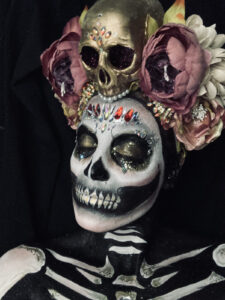 A model with skeleton bodypaint and skull face paint, with a head dress.