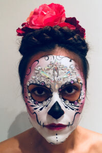 A woman with sugar skull makeup for Halloween, using face paint and decorative gemstones.
