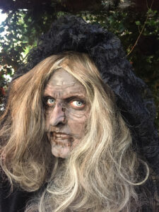 A woman made up as a witch for Halloween, using face paint and prosthetics.