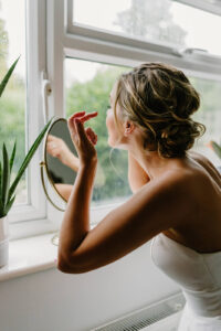 A bride adjusting makeup in a mirror.