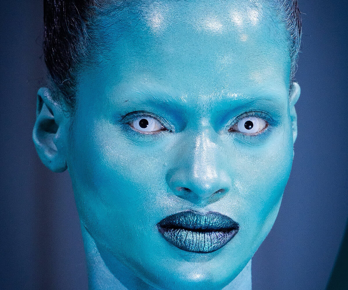 A model with white contact lenses and a shiny blue face for London Fashion Week 2024.