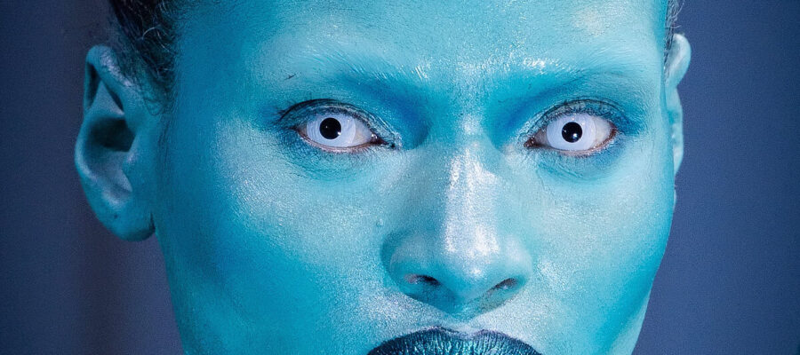 A model with white contact lenses and a shiny blue face for London Fashion Week 2024.