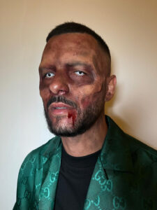 A man with zombie makeup and prosthetic cheekbones.