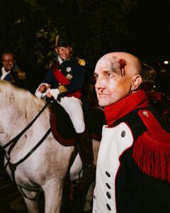 French Revolution soldiers, one on a horse, with makeup showing facial wounds and bleeding.