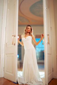 Blonde bride in white dress walking through a door.