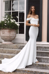 Pretty bride with off-the-shoulder dress standing on steps.