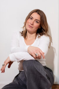 Makeup artist in white top and crossed arms smiling at camera.